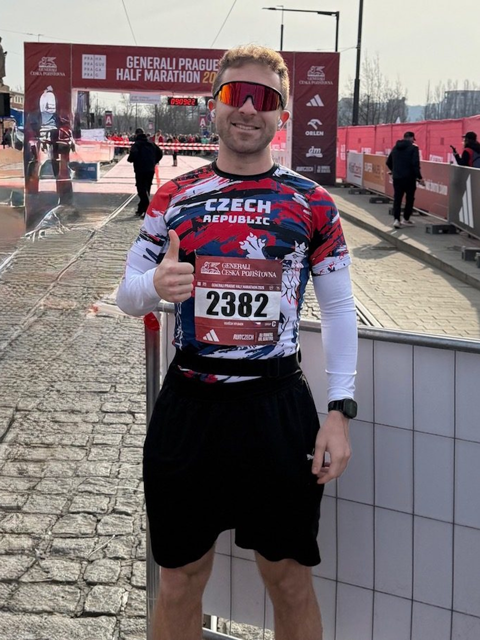 Běžec se startovním číslem a sportovními brýlemi před cílovým prostorem závodu