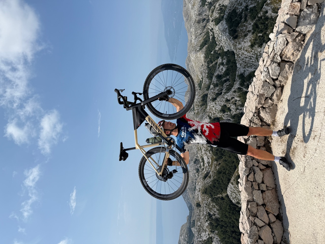 Cyklista drží jízdní kolo na vyhlídce nad hornatou krajinou