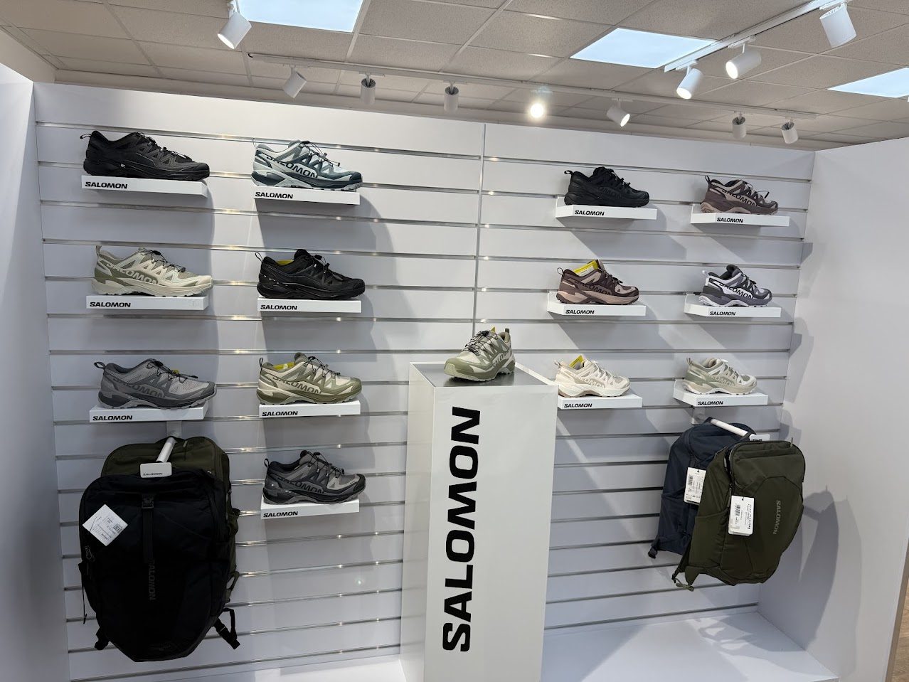 Stěna s modely sportovní obuvi a batohy značky Salomon